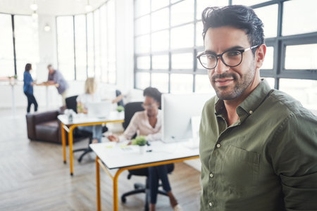 I face challenges head-on. a male designer in a office with his colleagues in the background.の写真素材