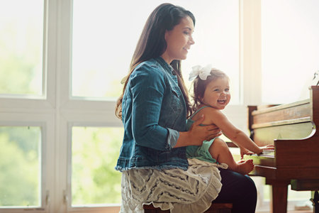 Learning as she grows. a mother playing the piano with her adorable little daughter at home.の写真素材