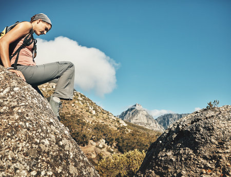 Setting off to greater heights. a young woman climbing over rocks while out on a hike through the mountains.の写真素材
