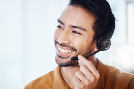 Asian man, call center and smile with headphones for customer service, consulting or support at office. Happy male consultant or agent smiling in telemarketing with headset for online advice or helpの写真素材