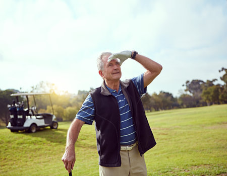 Admiring his shot. a senior man shielding his eyes from the sun while playing golf.の写真素材