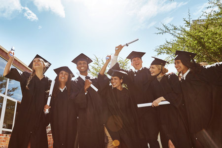 Celebrating graduation. Portrait of a group of smiling university students holding their diplomas outside on graduation day.の写真素材