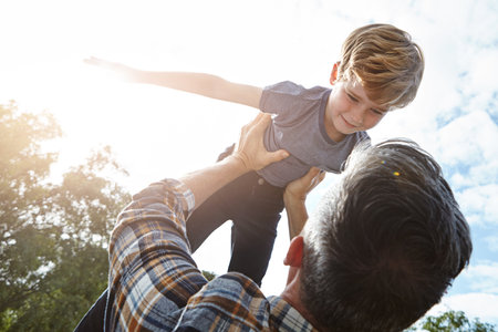 Raising kids is a privilege and pleasure. a father lifting his son high into the air.の写真素材