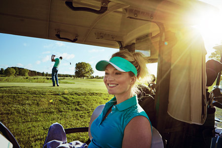 How can you not be happy when youre golfing. woman sitting in a golf cart on the fairway.の写真素材