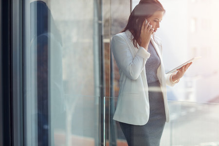 Staying connected in more ways than one. a young businesswoman using a phone and digital tablet in an office.の写真素材