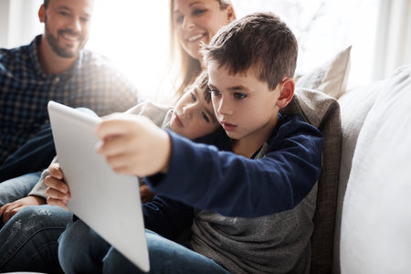 The tech way of keeping the kids entertained. two adorable brothers using a digital tablet together with their parents on the sofa at home.の写真素材