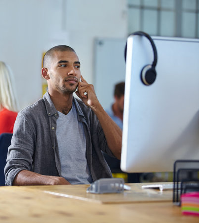 Im sure we can make that work. a designer talking on a cellphone while working on a computer in an...