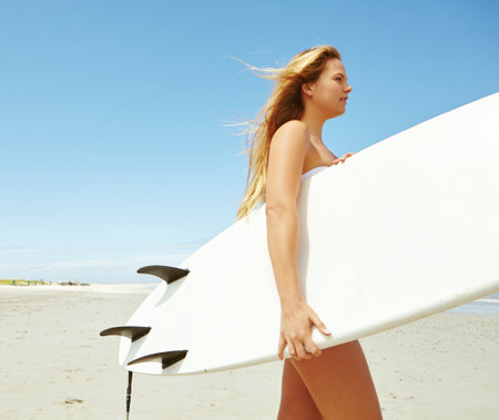 Surfing beauty. a young female surfer carrying her surfboard on the beach.の写真素材