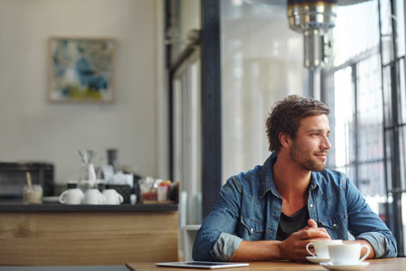 Contemplating things over coffee. a handsome young man looking thoughtful while having coffee at a cafe.の写真素材