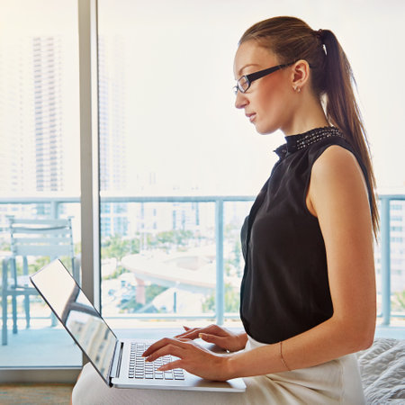 Checking in with the office. A young businesswoman working on her laptop in her hotel room.の写真素材