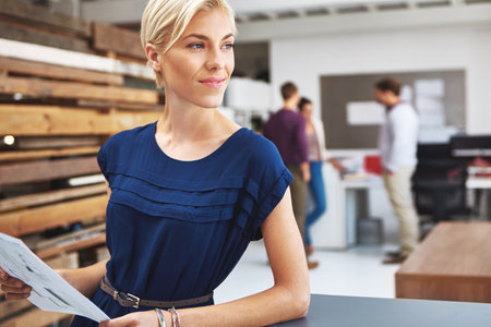 Contemplating success. a young female designer looking over some paperwork with her colleagues in the background.の写真素材