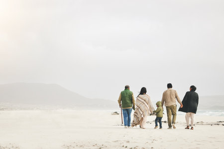 Children, holding hands and family walking at the beach in winter for quality time, love and care outdoor. Men, women or grandparents with parents and kids with mockup on a travel vacation in winterの写真素材