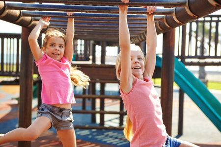 Children need the freedom and time to play. two little girls hanging on the monkey bars at the...