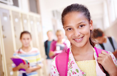 Ready for the bell. Portrait of a young school girl with her friends standing in a hallway in the background.の写真素材