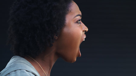 Use your voice as your weapon. a woman shouting against a dark background.の写真素材