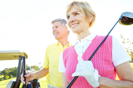 Enjoying their golf day. Attractive elderly couple with their golf clubs over their shoulders.の写真素材