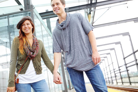 A couple that travels together, stays together. A couple holding hands and walking in a train station with copyspace.の写真素材