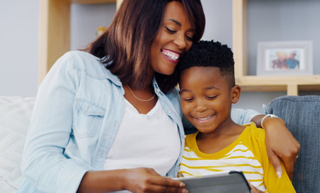 Watching some of our favorite videos together. an adorable little boy using a digital tablet with his mother while spending quality time together at home.の写真素材