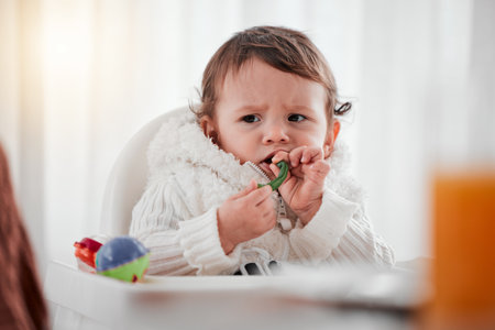 Baby, angry child and eating vegetables in home for health, wellness and nutrition. Upset kid, high chair and food, veggies or breakfast in kitchen for healthy diet, growth and development in house.の写真素材