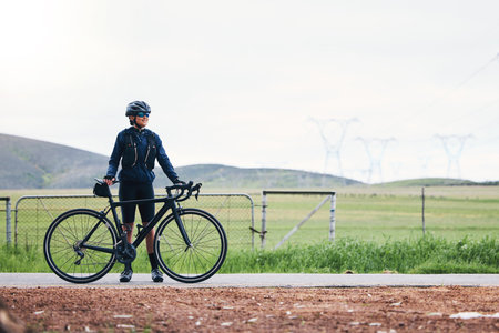 Woman, athlete and bicycle in countryside, mockup on sky and training for triathlon, sports and goals. Female cyclist, bike and fitness gear with motivation, freedom or thinking of cardio performanceの写真素材