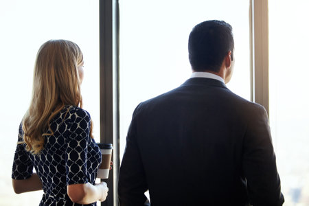 Enjoying the view together. Rearview shot of two young businesspeople standing in their office.の写真素材