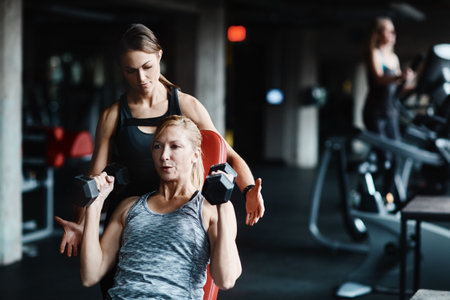 Getting fit with the best instructor. a mature woman lifting weights with a female instructor at the gym.の写真素材