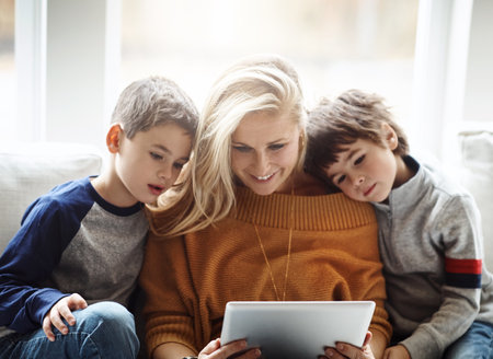 Incorporating screen time into family time. two adorable brothers using a digital tablet together with their mother while relaxing on the sofa at home.の写真素材