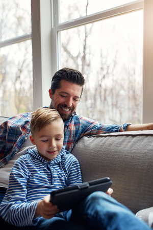 So young but he already knows so much. a little boy using a digital tablet with his father at home.の写真素材