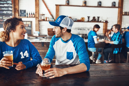 They found love in a sports bar. a young man and woman having beers while watching a sports game at a bar.の写真素材