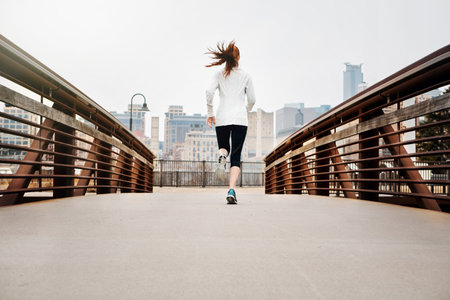 Running along the path to better health. Rear view shot of a sporty young woman running in the city.の写真素材