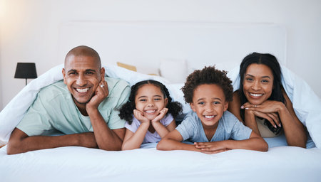 Portrait, family and smile in bedroom blanket in home, bonding and relaxing or lying. Bed, happiness and children with mother and father enjoying quality time together, having fun and care in house.の写真素材