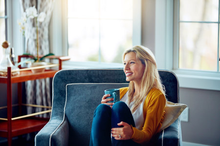 Take time to reflect. a young woman relaxing on her sofa with a cup of coffee.の写真素材