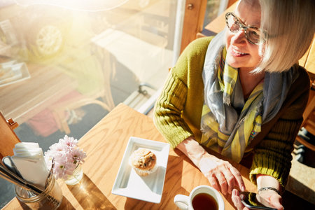 Its turning out to be such a beautiful day. a senior woman texting on her cellphone in a cafe.の写真素材
