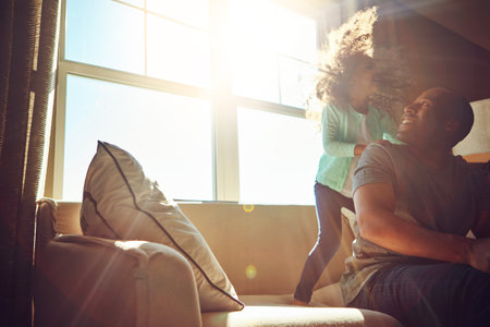 Shes all about having fun. a happy little girl playing with her father while he relaxes on the couch at home.の写真素材