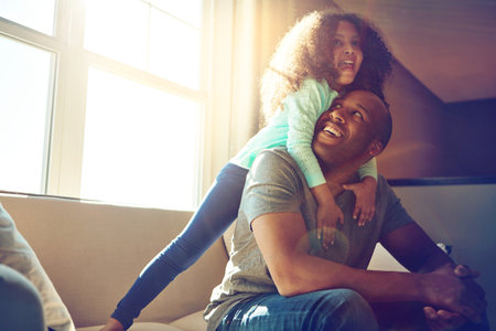 Fun is guaranteed when theyre together. a happy little girl playing with her father while he relaxes on the couch at home.の写真素材