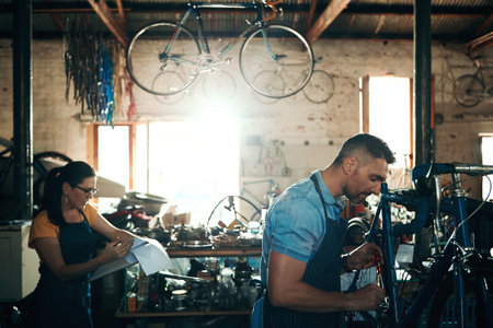 The team to keep your bicycle riding smoothly. a man and woman working together in a bicycle repair shop.の写真素材