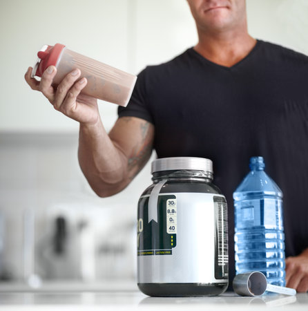Man, hands and protein shake for nutrition, muscle gain or body mass product and supplement on kitchen table. Hand of male bodybuilder preparing pre workout drink for exercise or healthy meal at homeの写真素材