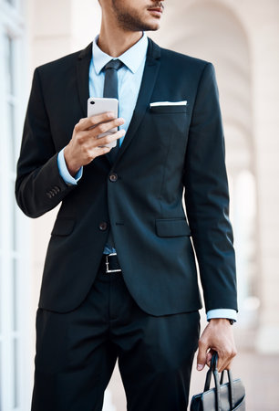 Contemplating while using his cellphone in the city. an unrecognizable businessman using a cellphone outside.の写真素材