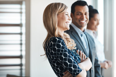 Only success can bring that kind of smile. a young businesswoman standing in an office with her colleagues in the background.の写真素材