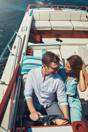 Is there a better place to start an adventure. High angle shot of an affectionate young couple sailing on the open seas in their yacht.の写真素材