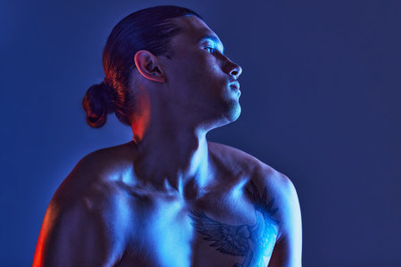 Man, sexy body and light in studio for art, fitness or beauty of a person on a blue background. Face, strong chest and fitness model with a tattoo, glow and creative motivation for aesthetic backdropの写真素材