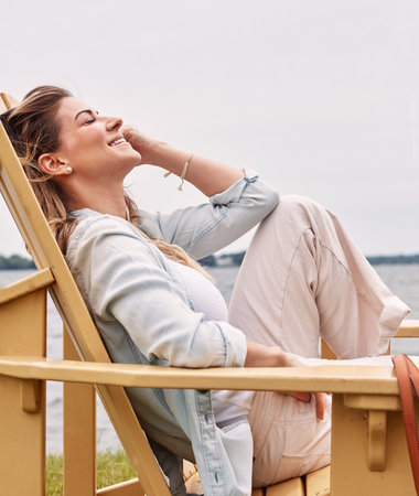 Theres no place for stress here. a beautiful young woman relaxing on a chair next a lake.の写真素材