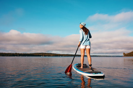 The beauty out here is breathtaking. a young woman paddle boarding on a lake.の写真素材