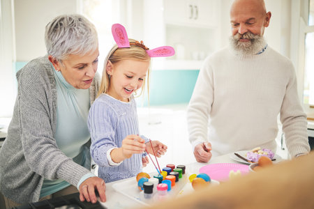 Easter, art and a girl painting with her grandparents in their home for love, bonding or celebration together. Family, kitchen or egg with a senior couple and their grandchild in a house to paintの写真素材