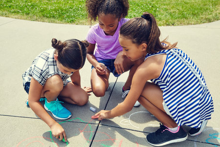 We want to make this pavement colourful. adorable little girls drawing with chalk on the pavement outdoors.の写真素材