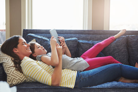 Learning the ins and outs of technology. a mother and her daughter using a digital tablet together on the sofa at home.の写真素材