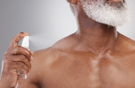Senior man with spray bottle, cologne and grooming with beauty and cosmetic fragrance isolated on studio background. Skin, cosmetics product and perfume deodorant with clean male person and hygieneの写真素材