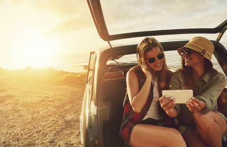 Roadtrip moments. two friends taking a selfie while sitting in the trunk of a car.