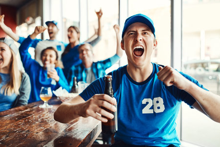 We won. a man cheering while watching a sports game with friends at a bar.の写真素材