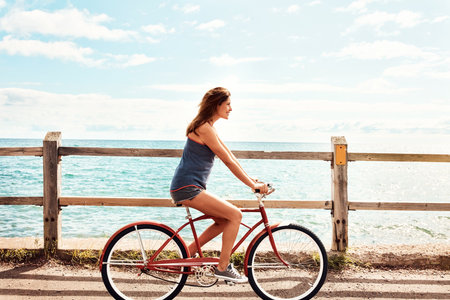 Fitness is a lifestyle. a beautiful young woman riding her bicycle on the promenade.の写真素材